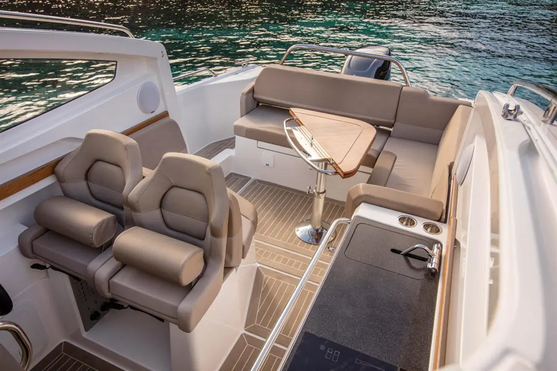 Luxury boat interior featuring beige seating, a wooden table, and a sleek kitchen area with modern fixtures.